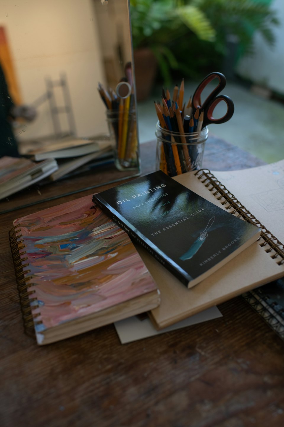 Art supplies on a wooden desk next to an oil painting textbook.
